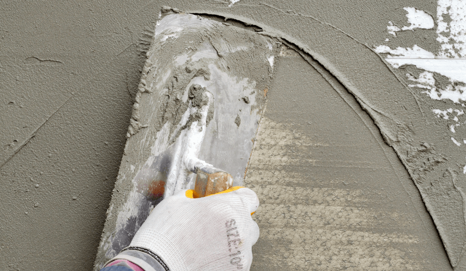 Close-up of stucco being applied to exterior wall near stone masonry base.